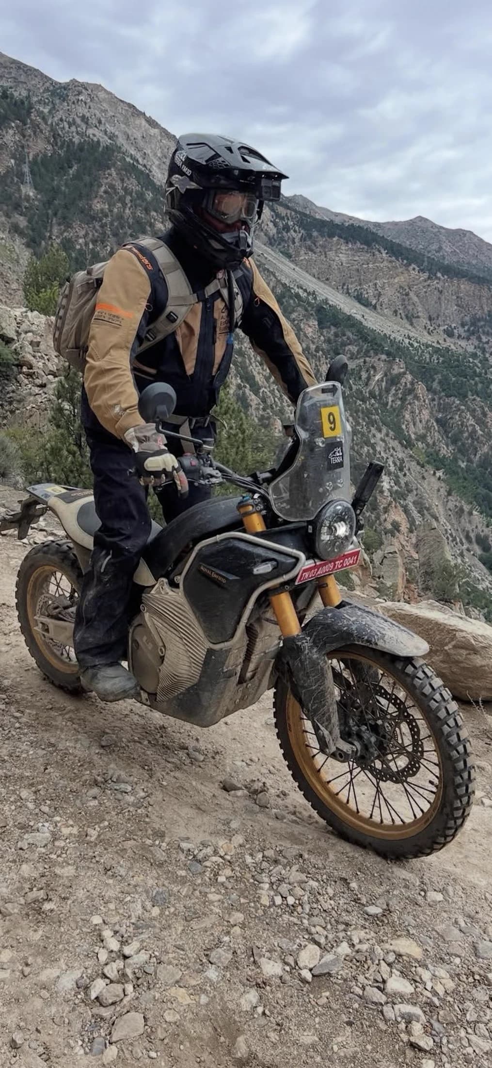 Rider standing on a loaded adventure bike overlooking the mountains