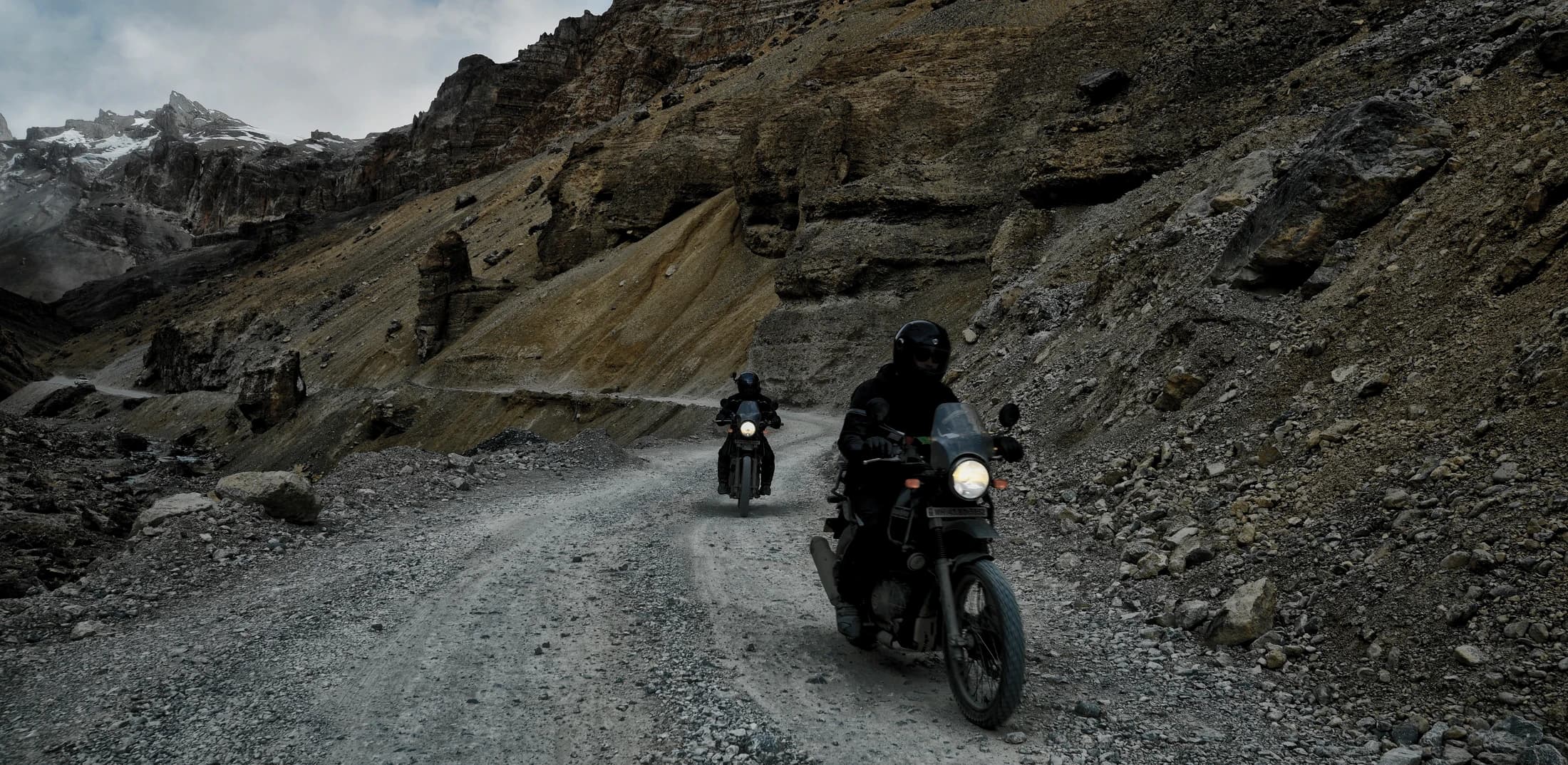 Two riders on Royal Enfield Himalayan adventure bikes climbing a mountain dirt road